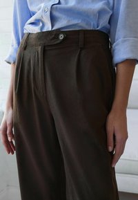 Bruine linnen broek met een hoge taille, zijzakken en een enkele knoopsluiting. Gekenmerkt door een lichtblauw shirt. Zachte textuur.