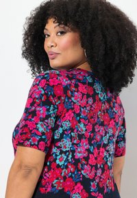 Vestido con estampado floral que presenta flores en tonos rosa, rojo y turquesa sobre un fondo marino. Mangas cortas, escote redondo y silueta ajustada.