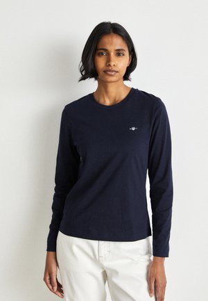 Maglietta a maniche lunghe blu navy in morbido cotone con scollatura a girocollo. Presenta un piccolo logo sul lato sinistro del petto e una vestibilità comoda.