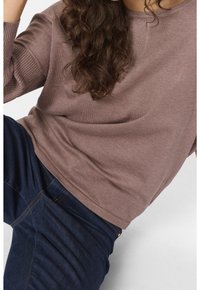 Maglione a maglia color marrone chiaro con polsini a coste, abbinato a jeans blu scuro. Il maglione ha una vestibilità comoda e una texture liscia.