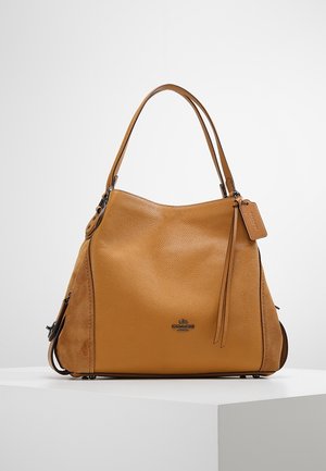 Tan leather and suede handbag with double handles, Coach logo, and attached leather tag, displayed on a white surface.