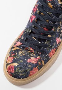 Baskets à motif floral avec une tige en tissu bleu marine, ornées de fleurs roses et jaunes, des lacets noirs et une semelle en caoutchouc gomme.