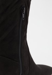 Schwarze Wildlederstiefel mit einem seitlichen Reißverschluss zum Verschließen. Die Textur ist glatt, mit einer passgenauen Form, die sich dem Bein anpasst.