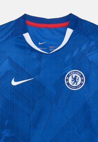 Blå Nike fotballtrøye med rund hals, hvite og røde detaljer, teksturert mønster og Chelsea fotballklubb-logo på brystet.