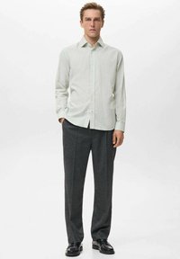 Camisa de botones a rayas verde claro combinada con pantalones de vestir gris oscuro, con un corte recto y una textura de tela suave. Zapatos negros.