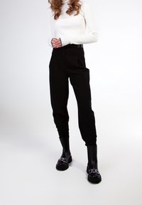 Pantalons noirs taille haute à jambes fuselées, associés à un haut col roulé blanc à côtes et des bottes épaisses noires avec des éléments en métal argenté.