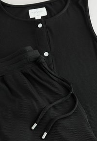 Czarna, prążkowana bluzka bez rękawów z okrągłym dekoltem i detalem w postaci guzików, w zestawie z dopasowanymi czarnymi spodniami z regulowanym paskiem na drawstring.