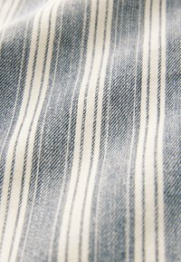 Niebiesko-biała tkanina w paski o teksturze przypominającej dżins; posiada cienkie pionowe paski na miękkim, tkanym podłożu.