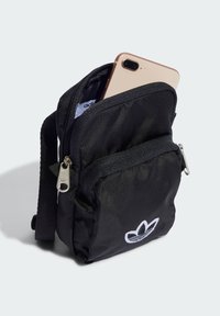 Svart nylon tvärs över axeln-väskan med ett dragkedjefack som rymmer en smartphone, med vit logotypbroderi och ett silvrigt dragkedjehandtag.