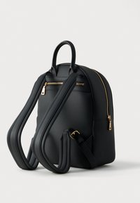 Μαύρο σακίδιο πλάτης από λείο συνθετικό υλικό, με χρυσά φερμουάρ, μπροστινή θήκη, ρυθμιζόμενους ιμάντες και στρογγυλεμένο σχήμα.