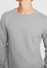 Pull gris texturé avec un design côtelé, col rond et manches longues, fabriqué en tissu tricoté doux.