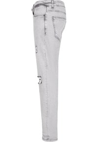 Jean en denim gris avec une coupe slim, des détails déchirés et un design classique à cinq poches. Texture lisse et jambes fuselées.