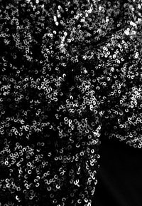 Țesătură neagră cu paiete sclipitoare, circulare, dispuse strâns una lângă alta, creând o suprafață texturată împotriva unui fundal întunecat.