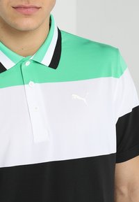 Polo vert, blanc et noir avec un design à trois bandes. Comprend un col et un petit logo Puma blanc sur la poitrine.