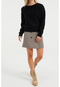 Černý svetr s texturovaným vzorem, doplněný hnědou sukní v psím zubech s předními knoflíky a béžovými šněrovacími botami.