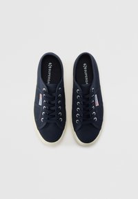 Námornícky plátené tenisky s kulatou špičkou, bílou podrážkou a kontrastními šněrovacími otvory. Obsahují logo Superga na jazyku a boku.