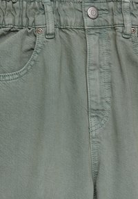 Gros plan sur un pantalon en denim vert clair avec une taille élastique, un bouton à l'avant et des poches avec des rivets en métal et le logo Pull&Bear.