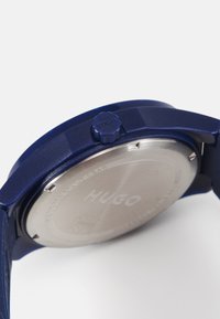 Reloj de silicona azul con fondo de acero inoxidable, que cuenta con una corona azul texturizada y el nombre de la marca en relieve. Impermeable hasta 8 bares.