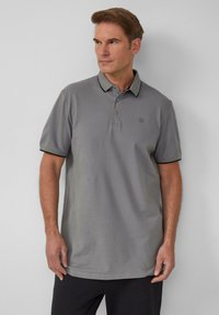Grijze polo met een gladde stof, voorzien van een kraag, een drieknoopssluiting en contrasterende zwarte afwerking op de mouwen en kraag.