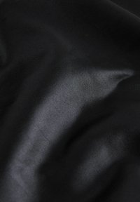 Tessuto nero con una superficie liscia e una leggera lucentezza, caratterizzato da pieghe delicate e un colore profondo e uniforme.