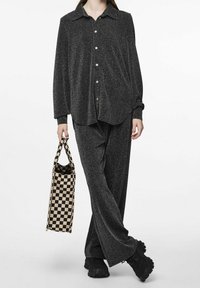 Camicia nera scintillante con bottoni abbinata a pantaloni neri. Accentuata da una borsa a rete a scacchi e sneakers nere.