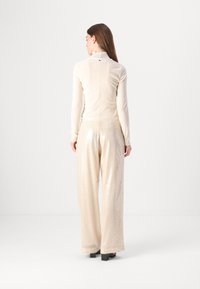 Lichtbeige, aansluitend longsleeve top met een gerimpelde kraag en doorzichtige textuur; gecombineerd met wijde, glanzende broek in een bijpassende kleur.