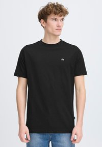 Tricou negru din bumbac cu guler rotund și mâneci scurte. Prezintă un mic logo alb pe piept. Purtați cu blugi albaștri.