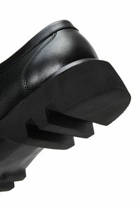 Zwarte leren schoen met een dikke, geribbelde rubberen zool. De hak heeft diepe gripgroeven en een glad bovenwerk met minimale stiksels.
