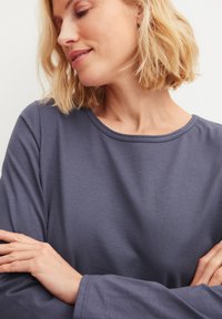 Langärmeliges Hemd in Dunkelblau mit Rundhalsausschnitt und weichem, glattem Stoff. Arme verschränkt, betont die lässige Passform.