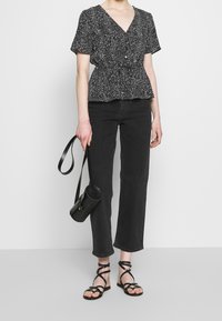 Černobílá vzorovaná blůza s krátkým rukávem a výstřihem do V, spárovaná s černými džíny rovného střihu a černými sandály na podpatku.