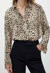 Cremefarvet skjorte med knapper og brun leopardprint, med lange ærmer og løs pasform, parret med højtaljede sorte jeans.