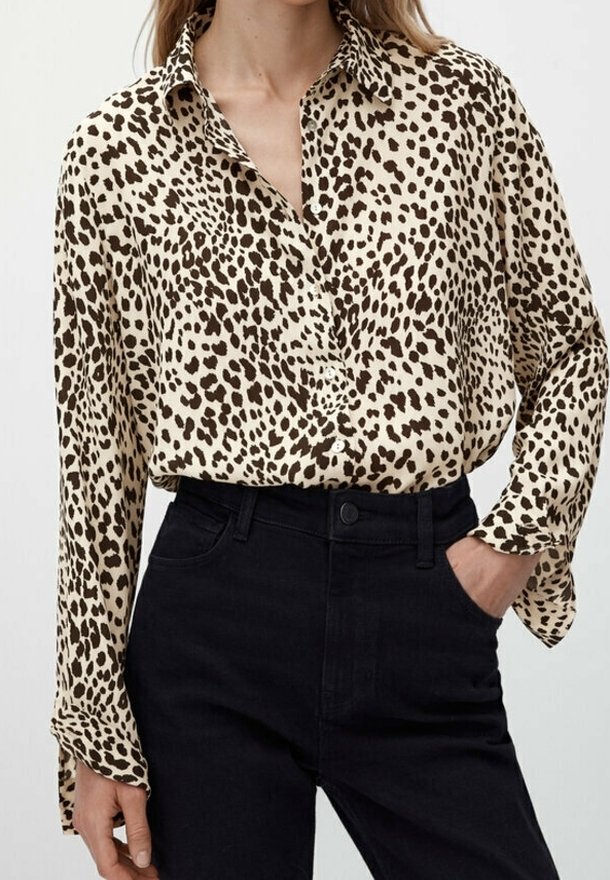 Cremefarvet skjorte med knapper og brun leopardprint, med lange ærmer og løs pasform, parret med højtaljede sorte jeans.