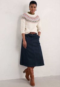 Sweater crema con bodoque estampado, falda larga de mezclilla oscura y botas marrón hasta la rodilla. Incluye un cinturón marrón y detalle de tejido texturizado.