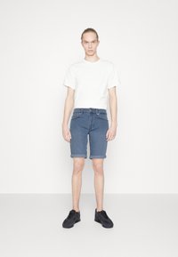 Pantalones cortos de denim en azul medio con dobladillo, combinados con una camiseta blanca sencilla y zapatillas negras. Diseño simple con un corte recto.