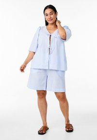 Completo a due pezzi a righe blu chiaro, caratterizzato da una maglietta dal fit morbido con un nodo frontale e maniche corte, abbinato a pantaloni corti coordinati, realizzati in tessuto morbido.