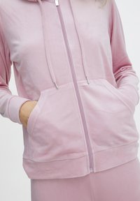 Lys pink zip-up hoodie lavet af blødt, tekstureret stof med hætte, sidelommer og sølv lynlås detaljer.