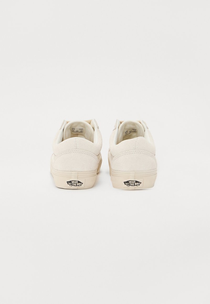Zapatillas de ante blancas con un diseño de corte bajo, que presentan una suela de goma en color crema y el logo "Off the Wall" de Vans en el talón.