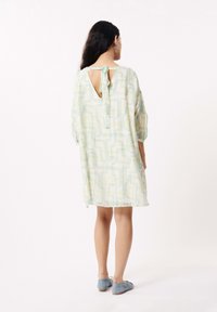 Lichte, gebloemde jurk in pastelkleuren met groene en blauwe geometrische ontwerpen. Heeft een strik aan de achterkant en een ronde halslijn, ontspannen pasvorm.