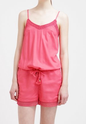 Femme portant un débardeur rose avec des détails en crochet et un short assorti avec une taille à cordon et un bord en dentelle sur les jambes.
