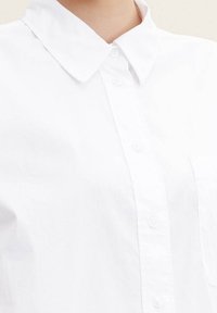 Weißes Button-up-Shirt mit klassischem Kragen, aus leichtem Stoff gefertigt. Verfügt über eine einzelne Brusttasche und eine verdeckte Knopfleiste.