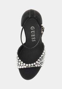 Scarpa nera con tacco alto, con una finitura texturizzata, decorata con borchie metalliche argento lungo la cinghia, dotata di chiusura alla caviglia con fibbia.