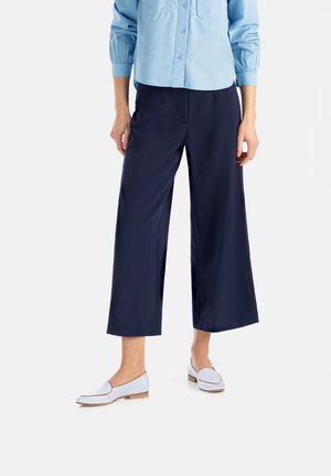 Pantaloni a gamba larga blu navy realizzati in tessuto morbido, abbinati a scarpe azzurro chiaro con un design discreto e tacco basso.