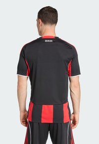 T-shirt de sport noir avec des rayures rouges, manches courtes et col blanc. Le texte dans le haut du dos indique "NUR EINE STADT. NUR EIN VEREIN."
