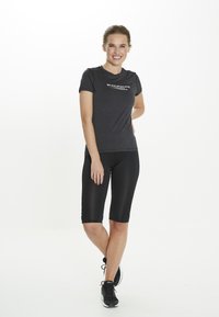 Sort atletisk T-shirt med en subtil tekstur og frontlogo, parret med sorte knælange kompressionsshorts og sorte atletiske sko.