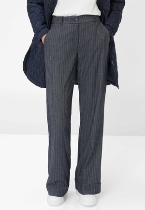 Navy pinstriped trousers with a loose fit, featuring a flat front, belt loops, side pockets, and a crease down the legs. White sneakers visible.