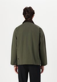 Olive green jacket with a dark brown corduroy collar, featuring a relaxed fit, raglan sleeves, and snap-button details on the sides.