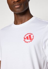 White cotton t-shirt featuring a red circular logo with three stripes and the text "ADIDAS FOOTBALL" in bold lettering on the chest.