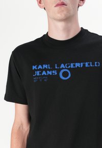 Svart bomull t-skjorte med blå grafisk tekst med "KARL LAGERFELD JEANS" og et rundt logo, rund halslinning og korte ermer.