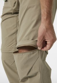 Beige cargo nadrág, cipzáros nyílással a térdnél, sima tapintású és varrott varratokkal. A dizájn lehetővé teszi az állítható hosszúságot.