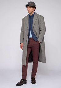 Šedý vlněný kabát, modrá prošívaná bunda, modrá košile, vínové kalhoty a tmavě hnědé boty. Doplněno šedou čepicí a knoflíkovými detaily.